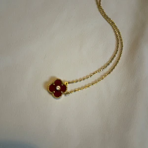 Guldigt halsband med röd blomma - Supersött halsband med tunn guldfärgad kedja och ett hänge i form av en röd blomma med guldkant och en liten pärla i mitten. Perfekt statement-piece för dig som gillar färg och unika detaljer.