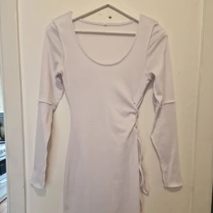 Vit långärmad klänning med snörning - Supersnygg vit långärmad klänning med rund halsringning och cool snörningsdetalj i sidan. Perfekt för dig som gillar stilrena och trendiga plagg.