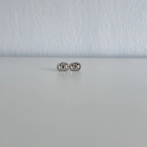 Silverfärgade örhängen med diamanter  - Ett par silverfärgade örhängen med diamanter på från DAZZLING som man ser på bilderna är använda ett par gånger och har med tiden blivit missfärgade/tappat färgen även plupparna, alltså inte äkta silver! Har försökt rengöra dom så gått det går. Köptes för 69kr! FÖRST TILL KVARN!