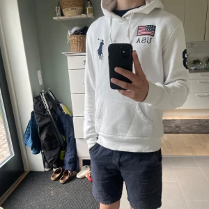 Vit Ralph Lauren big pony hoodie - Vit hoodie från Polo Ralph Lauren med broderad USA-flagga, texten 'USA' och 'UNITED STATES', samt stor marinblå polospelare på bröstet. Nummer 3 på ärmen och ryggen. Klassisk känguruficka och huva. Storlek M passar XS. Jag på bilden är 170cm. Den är i bra skick är endast lite missfärgad. 