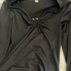 Svart långärmad topp från H&M XS - Svart långärmad topp från H&M i storlek XS. Toppen har en snygg rynkad detalj med liten öppning framtill vid bysten och en åtsittande passform. Perfekt att styla med jeans eller kjol för en trendig look.