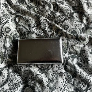 Silverfärgad kuvertväska med kedja - Riktigt snygg kuvertväska i metallic silver med stilren, rektangulär form och lång kedjerem. Väskan har ett hårt skal och stängs med ett metallspänne upptill. Kedjan går att ta bort. Köpt på glitter. Använd en gång. Går att mötas upp i Norrköping 😊
