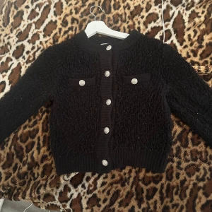 Svart kofta med silvriga knappar H&M XS - Mysig svart kofta från H&M i storlek XS. Koftan har en fluffig, stickad känsla, rund halsringning och snygga silvriga knappar framtill samt dekorativa fickor på bröstet. Perfekt för lager-på-lager och en chill men ändå stilsäker look.