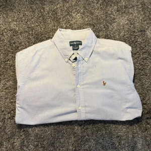 Ljusblå skjorta från Ralph Lauren - Klassisk ljusblå skjorta från Ralph Lauren med button-down krage och broderad logga på bröstet. Skjortan har långa ärmar och knäppning framtill. Perfekt för en stilren och avslappnad look., sitter som M! 🤩 pris 449