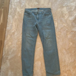 Lee West ljusblå jeans W34 L32 - Säljer ett par klassiska ljusblå jeans från Lee i modellen West. Jeansen har raka ben, fem fickor och Lee-logga på bakfickan. Tillverkade i bomull med snyggt slitna detaljer och normal passform. Perfekta till sneakers eller boots.