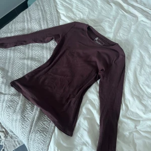 Brun långärmad topp S - Slimmad långärmad topp i mörk brun  färg. Tröjan har rund halsringning och är tillverkad i mjuk, ribbad bomull som sitter snyggt mot kroppen. Perfekt att styla med jeans eller kjol för en clean look.