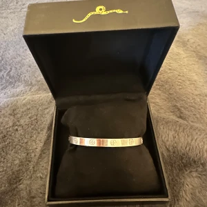 Cartier liknande armband i silver  - Stilrent armband silver. Armbandet är stelt och har en minimalistisk design som passar perfekt till din outfit. Levereras i original ask med guldfärgad orm-detalj på locket.