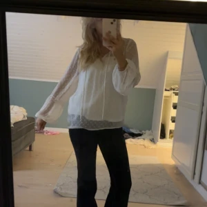 Vit prickig blus med volymärmar - Supersöt vit blus med transparenta, långärmade volymärmar och prickigt mönster. Blusen har knytband vid halsen och fina spetsdetaljer på ärmarna. Perfekt för dig som gillar en romantisk och luftig stil.