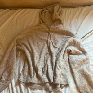 Beige stickad hoodie med huva -  stickad hoodie med huva och snörning. Tröjan har långa ärmar och ribbade muddar vid ärmslut och nederkant. 