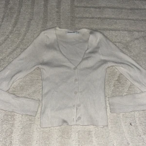 Beige ribbad kofta från Kappahl - Säljer en beige ribbad kofta från Kappahl med v-ringning och knappar framtill. Koftan har lång ärm och är figurnära i modellen, perfekt att slänga över en topp eller klänning. Superenkel att matcha till olika outfits!