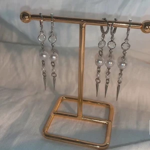 Silverörhängen med pärlor och spikes - Snygga långa örhängen i silverfärg med kedjor, vita pärlor och coola spetsiga spikes längst ner. Ger en edgy vibe med mixen av pärlor och metall. Perfekta för dig som vill sticka ut med dina accessoarer.