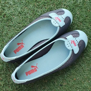 Grå och ljusblåa ballerinaskor Puma flats - Snygga ballerinaskor från Puma i grått och ljusblått med coola detaljer och röd Puma logga framtill. Skorna har rund tå, platt sula och är tillverkade i en mix av syntet och textil. Perfekta för dig som vill ha en sportig och stilren look. Fint skick förutom mindre fläck vid häl!