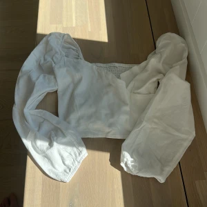 Vit croppad blus med puffärm - Säljer en vit croppad blus med långa puffärmar och resår vid ärmslut och midja. Toppen har en fyrkantig ringning och är perfekt för dig som gillar romantisk och trendig stil. Passar snyggt till både jeans och kjol.