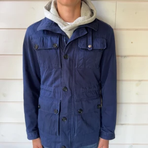J.lindeberg field jacket navy - Hej, säljer en superfin j.lindeberg field jacka i storlek S. Jackan är mycket bra skick och har inga hål eller tydliga fläckar. På bakre sidan av kragen är den lite missfärgad se bild. På ena armen har en knapp blivit halv men fungerar fortfarande som vanligt och tänks ej på vid användning. Hör gärna av er vid frågor och funderingar! Pris går att diskuteras vid smidig och snabb affär!🤝