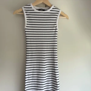 Randig långklänning i ribbad bomull - Snygg ärmlös långklänning från Bik Bok i vit ribbad bomull med svarta horisontella ränder. Klänningen har en tight passform och en liten slits bak. Storlek Xs. 🌸✨