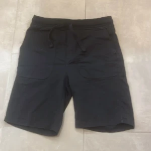 Svarta shorts med snörning från OVS - Svarta shorts från OVS med elastisk midja och snörning för skön passform. Modellen har två stora fickor framtill och är gjorda i mjukt bomullsmaterial. Perfekta för chill dagar eller när du vill ha det bekvämt.