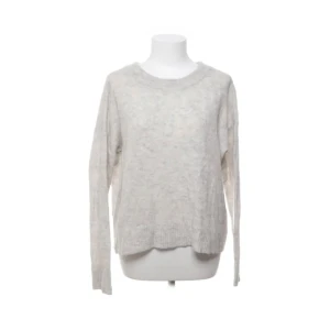 Ljusgrå stickad tröja - Mysig ljusgrå stickad tröja med rund hals och långa ärmar. Tröjan har en avslappnad passform och ribbade muddar vid ärmslut och nederkant. Perfekt för lager-på-lager under kyliga dagar.