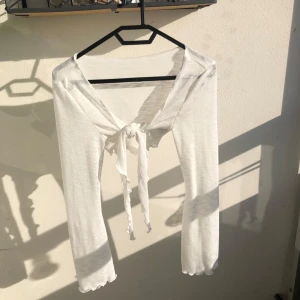 Vit långärmad tunn kofta med knyt - Superfin vit tunn långärmad kofta . Tröjan har knyt framtill och vågiga kanter vid ärmslut . Jättefin att knyta lver bikinin på stranden.