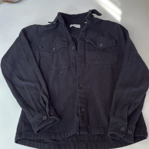 Svart overshirt från Jack & Jones M - Svart overshirt från Jack & Jones Premium i storlek M. Skjortan har två bröstfickor med knappar, klassisk krage och långa ärmar med manschett. Tillverkad i mjuk bomull, perfekt att bära som lager över t-shirt eller hoodie.