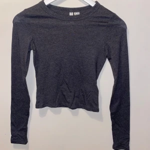 Mörkgrå långärmad topp H&M Divided - En basic mörkgrå långärmad topp från H&M Divided. Modellen är figurnära med rund halsringning och tillverkad i mjuk bomullsblandning. Perfekt att styla med jeans eller kjol för en clean look.