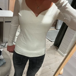 Vit långärmad tröja - Säljer en vit ribbad långärmad topp från H&M i storlek S. Toppen har en snygg v-ringning och sitter figurnära. Perfekt till jeans eller kjol och funkar året runt. Materialet är mjukt och stretchigt för en bekväm känsla.