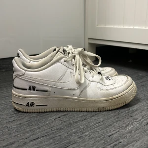 Nike Air Force 1 vita sneakers - Klassiska Nike Air Force 1 sneakers i helvitt skinn med svarta detaljer och logga. Lågt skaft, rund tå och snörning framtill. Lite smutsiga men inget fel på skicket alls 