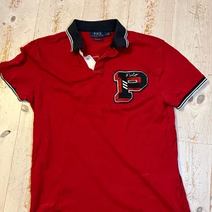 Röd Chief keef Piké Ralph Lauren - Röd t-shirt från Polo Ralph Lauren med svartvit krage och ärmslut. Stor broderad P-logga framtill och stor POLO New York-text på ryggen. Slim fit-modell i bomull. Pris kan diskuteras vid snabb affär