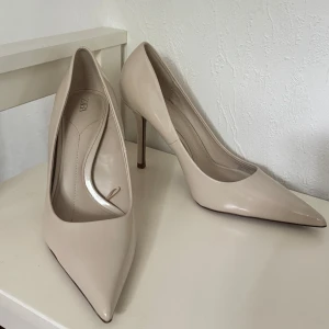 Beige pumps med spetsig tå från Zara - Stilrena pumps i blankt beige material från Zara. Skorna har spetsig tå och hög klack som ger en elegant siluett. Perfekta för dig som gillar en klassisk look med modern touch. Snygga att matcha med både jeans och klänning.