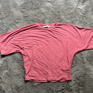 Rosa topp från 157 - En tight rosa topp från 157 i storlek XS. Modellen har breda, nästan fladdermusliknande ärmar och en tight passform runt midja. Tillverkad i mjuk bomull, perfekt för en chill och bekväm stil. Rund halsringning och enkel design utan mönster.
