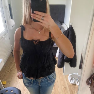 Svart linnetopp med knytband från H&M - Säljer en svart linnetopp med knytband på axlarna och liten rosett framtill. Toppen har en luftig och lätt rynkad design som ger en avslappnad känsla. Perfekt till jeans eller kjol för en cool och enkel look. Storlek L men sitter som en S.