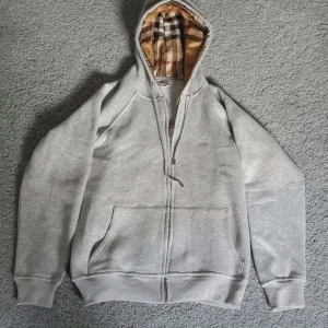 Grå hoodie från Burberry - Grå hoodie från Burberry med klassiska rut-designen i s  luvan. Storleken är M men passar som S. om ni har frågor/önskar fler bilder skriv till mig!