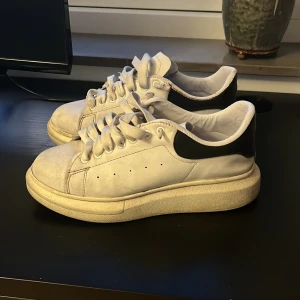 Alexander McQueen vita sneakers - Säljer ett par feta vita Alexander McQueen sneakers med svart häl och chunky sula. Skorna har klassisk snörning, rund tå och är gjorda i skinn. Perfekta för dig som vill sticka ut med en clean och stilren look. 2 hål i skorna därav priset 