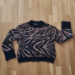 Zebramönstrad stickad tröja H&M - Säljer en stickad tröja från H&M i storlek S med snyggt zebramönster. Tröjan har lång ärm, ribbade muddar och en lite högre hals.