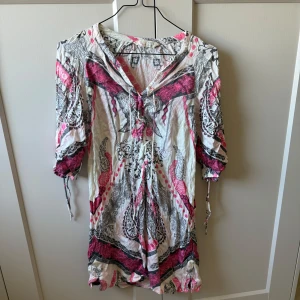 Mönstrad kortklänning Odd Molly - Supersöt kortklänning från Odd Molly med unikt paisleymönster i rosa, svart och vitt. Klänningen har snörning framtill, trekvartsärm med knyt och lätt v-ringning. Perfekt att ha som strandklänning!