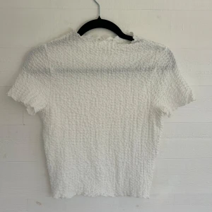 Vit kortärmad topp - Superfin vit topp med korta ärmar och ribbad, bubblig struktur. Den har en lätt croppad passform och vågiga kanter vid ärmslut och hals. Perfekt för dig som gillar en enkel men ändå unik stil. Klippt bort lappen men skulle säga att den passar storlek S🤩💕