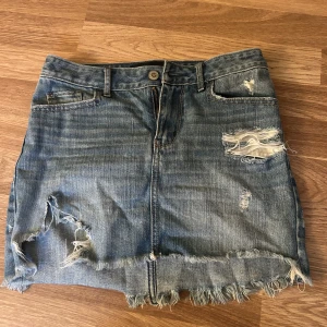 Hollister jeans kjol  - Snygg kort jeanskjol i blå denim med slitna detaljer och fransig nederkant. Kjolen har klassiska fickor fram och bak samt dragkedja och knapp framtill. Perfekt för en avslappnad och trendig look.