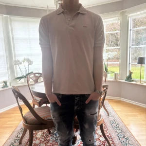 Rosa kortärmad piké från Hugo BOSS - Säljer en stilren rosa pikétröja från BOSS med klassisk krage och knappar framtill. T-shirten är kortärmad och har en diskret BOSS-logga på bröstet. Perfekt för dig som gillar en clean och enkel look.