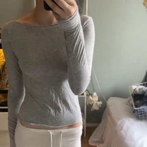 Ljusgrå långärmad topp - Slimmad och enkel ljusgrå långärmad topp med rundad halsringning. Sitter tajt mot kroppen och är tillverkad i ett mjukt, stretchigt material som känns skönt mot huden. Perfekt att styla med jeans eller kjol för en clean look.