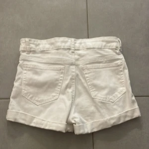 Vita jeansshorts med uppvik - Snygga vita jeansshorts med klassisk femficksmodell och uppvikta benslut. De har bälteshällor och stängs med knapp och dragkedja. Perfekta för varma dagar och en clean look.