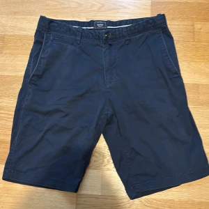Mörkblå shorts från Baxter - Snygga mörkblå shorts från Baxter i regular fit. Klassisk design med fickor på sidorna och bälteshällor. Tillverkade i bomull för en skön känsla och perfekt för varma dagar. Passar dig som gillar stilrena och enkla plagg. Det är bara att höra av sig vid minsta lilla fundering 🤔 