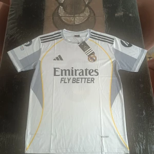 Real Madrid tröja  - Snygg Real Madrid fotbollströja från Adidas i storlek L med Mbappé och nummer 9 på ryggen. Tröjan är vit med grå och gula detaljer, svarta Adidas-ränder på axlarna och klubbmärke på bröstet. Materialet är lätt och andas, perfekt för match eller träning.