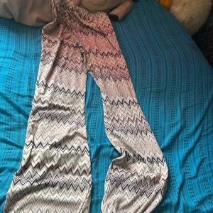 Mönstrade vida byxor från Kappahl - Säljer ett par superbekväma vida byxor från Kappahl med snyggt zickzackmönster i beige, svart och persikotoner. Byxorna har hög midja och är gjorda i ett mjukt, stretchigt material som känns skönt mot huden. Perfekta för dig som gillar en chill och trendig stil.