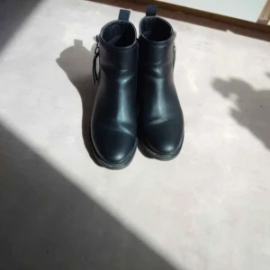 Svarta boots från Clou i skinn - Stilrena svarta boots från Clou i äkta skinn med rund tå och dragkedja på sidan. Snygg och enkel design med platt sula och diskreta detaljer, perfekta till jeans eller kjol. Storlek 40.