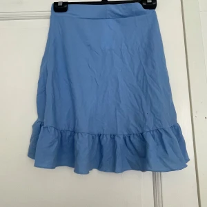 Blå volangkjol från Gina Tricot - Supersöt ljusblå kjol från Gina Tricot med volangkant nertill. Kjolen är kort och har en enkel, stilren design som passar perfekt till sneakers eller sandaler. Tillverkad i mjuk bomull som känns skön mot huden. Perfekt för vår och sommar!