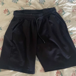 Svarta Nike shorts med snörning L - Svarta shorts från Nike i storlek L med elastisk midja och snörning. Klassisk sportig look med diskret Nike-logga på benet. Perfekta för träning eller chill dagar. Mjukt material och två sidofickor för extra funktion.