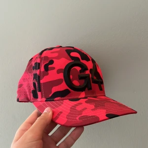 Röd camo keps från G/FORE - Snygg keps från G/FORE i röd och svart camouflage-mönster. Kepsen har en böjd skärm och stor 3D-logga framtill. Perfekt för dig som vill sticka ut med en sportig och trendig look.