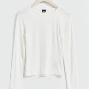Vit långärmad topp från Gina Tricot - Enkel och stilren vit långärmad topp från Gina Tricot. Modellen har rund halsringning och är tillverkad i mjuk, tunn bomullsmix som känns skön mot huden. Tröjan är aldrig använd men har lite inte så synliga fläckar på axlarna. 