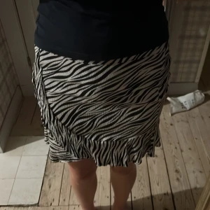Zebramönstrad kortkjol med volang - Snygg kortkjol med svartvitt zebramönster och volangkant. Kjolen har en elastisk midja. Säljs pågrund av att den är förliten. Den är köpt på Cubus.