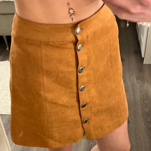 Brun manchesterkjol med knappar - Snygg kort brun kjol i manchester med silverfärgade knappar framtill i mycket bra skick!