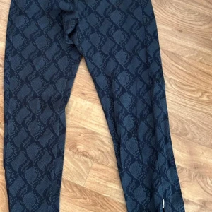 Champion leggings med ormmönster - Snygga svarta leggings från Champion med grått ormmönster. Modellen är tight och har en liten broderad Champion-logga vid benet. Perfekta för dig som vill sticka ut med ett coolt mönster och sportig vibe.